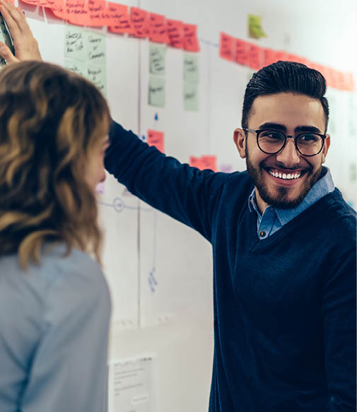 Positive young man laughing while collaborating with colleagues on creating presentation using colorful stickers for productive work in office Male and female students having fun during workshop